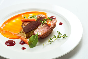 Appetizing confit duck breast with pear and yellow apple puree, berry sauce in a white plate. Isolated on grey background.