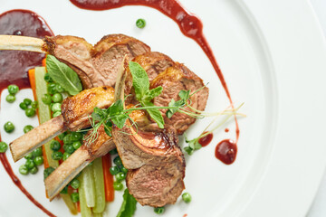 Appetizing grilled rack of lamb with vegetables and berry sauce in a white plate. Grey on white background.
