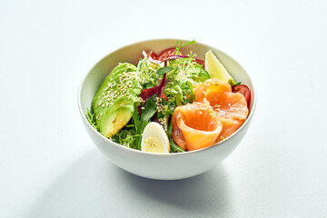 Delicious veggie bowl with salmon, avocado, cucumber, cherry tomatoes and mix salad in a white plate. Isolated on grey background.