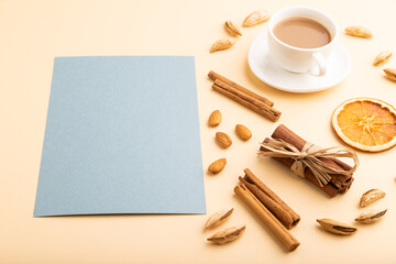 Obraz na płótnie Canvas Composition with gray paper sheet, almonds, cinnamon and cup of coffee. mockup on orange background. side view, copy space.