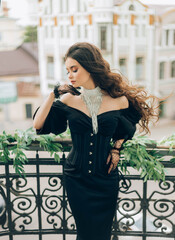 glamorous woman in black evening dress puffy sleeves stands on vintage balcony. fashion model...
