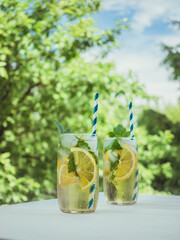 Cold lemonade with ice and currant leaves in the garden on a wooden table. Background - blue sky and green foliage of trees