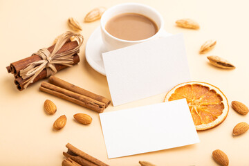 Composition of white paper business cards, almonds, cinnamon and cup of coffee. mockup on orange background. side view, copy space.