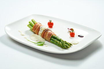 Grilled asparagus with bacon and mustard sauce in a white plate. Isolated on gery background.