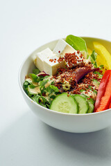 Delicious veggie bowl with cucumber, bell pepper, salad mix, quinoa and tofu in a white plate. Isolated on grey background.