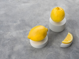 The concept of an unusual still life of lemons on gray plaster coasters and podiums on a gray concrete background. A whole lemon in a lying, standing position and a lemon wedge.  Copy space
