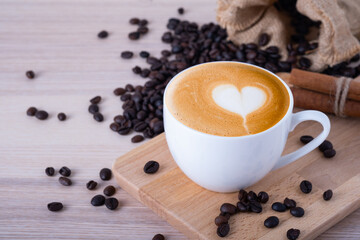A glass mug of hot latte coffee art with coffee beans and props on wooden table. Breakfast in the morning love coffee break concept. Copy space for text.