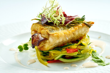 Serving of grilled sea bass with vegetables in a white plate. Isolated on grey background.