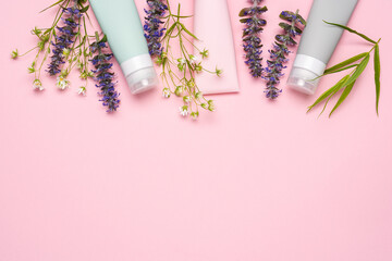Cosmetic tubes on pink background with wild flowers and plants. Natural organic cosmetics