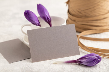 Gray paper invitation card, mockup with purple crocus snowdrop flowers on gray concrete background. side view, copy space.
