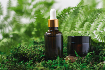 Beauty products on moss and stones podium. Serum and face care cream in glass bottles. Natural cosmetics concept