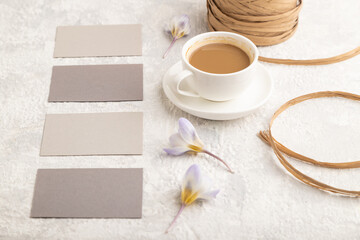 Obraz na płótnie Canvas Gray paper business card mockup with spring snowdrop crocus flowers and cup of coffee on gray concrete background. side view, copy space.