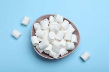 Fototapeta na wymiar Delicious puffy marshmallows on light blue background, flat lay