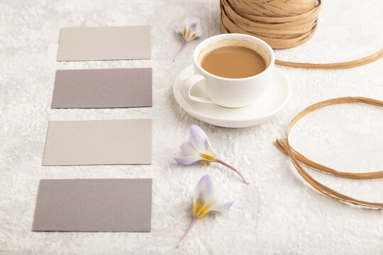 Gray paper business card mockup with spring snowdrop crocus flowers and cup of coffee on gray concrete background. side view, copy space.