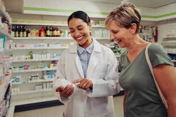 Muurstickers Young female pharmacist and customer reading ingredients and dosage in pharmacy standing near shelves © StratfordProductions