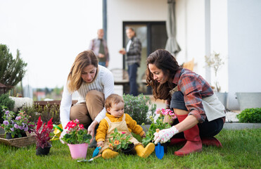 Happy multigeneration family outdoors planting flowers in garden at home, gardening concept.