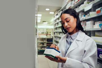 Woman checking medicine box reading expiry date and instructions standing in aisle of chemist