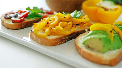 Vegan bruschetta. Delicious bruschetta with tomatoes, yellow peppers and avocado on a white plate. Appetizing Vegetable Snack Cheese Sandwiches