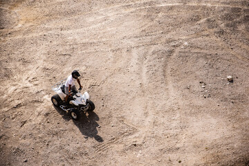 Person wearing a helmet and drifting on the sandy field with a quad bike