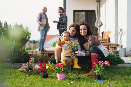 Happy Multigeneration Family Outdoors Planting Flowers In Garden At Home, Gardening Concept.