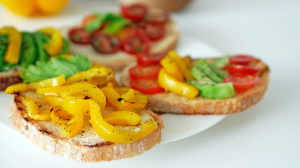 Vegan bruschetta. Delicious bruschetta with tomatoes, yellow peppers and avocado on a white plate. Appetizing Vegetable Snack Cheese Sandwiches