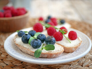 Sweet bruschetta with cream cheese and fresh berries. Homemade healthy breakfast with bread, cheese, blueberries and raspberries. Three delicious sandwiches on a plate
