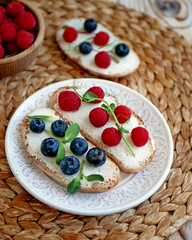 Sweet bruschetta with cream cheese and fresh berries. Homemade healthy breakfast with bread, cheese, blueberries and raspberries. Three delicious sandwiches on a plate