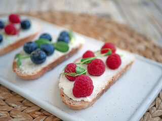 Sweet bruschetta with cream cheese and fresh berries. Homemade healthy breakfast with bread, cheese, blueberries and raspberries. Three delicious sandwiches on a plate