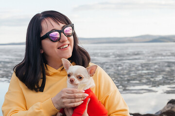 Portrait of a young brunette in nature with a Chihuahua dog in her arms.