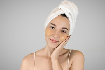 Beauty portrait of smiling woman in towel on head applying yellow nourishing mask on face on gray isolated background. Skin care concept. 