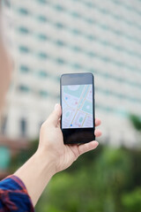 Close-up of unrecognizable man using GPS navigation on smartphone against modern building while searching for place