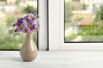 Vase with flowers near window on rainy day. Space for text