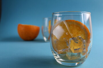 cooking lemonade with orange. step-by-step instructions. Step 1 pour into a glass of ice and put a piece of orange. Glass of ice and fruit orange on a blue background with a place for text