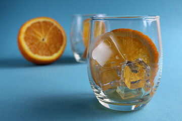 cooking lemonade with orange. step-by-step instructions. Step 1 pour into a glass of ice and put a piece of orange. Glass of ice and fruit orange on a blue background with a place for text