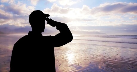 Fototapeta premium Composition of male soldier saluting over sea and blue sky