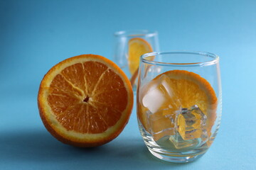 cooking lemonade with orange. step-by-step instructions. Step 1 pour into a glass of ice and put a piece of orange. Glass of ice and fruit orange on a blue background with a place for text