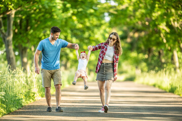 Happy family, father and mother enjoying a walk in the park with their little daughter