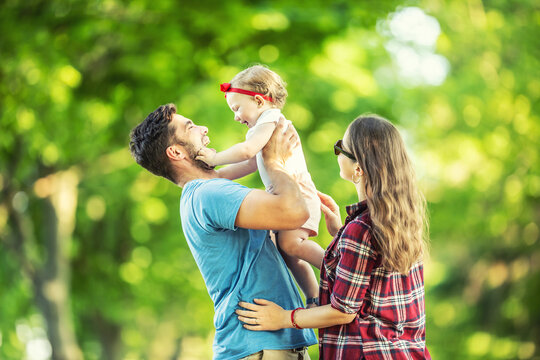 Happy family, father, mother and daughter are playing in the park and enjoying a sunny summer day