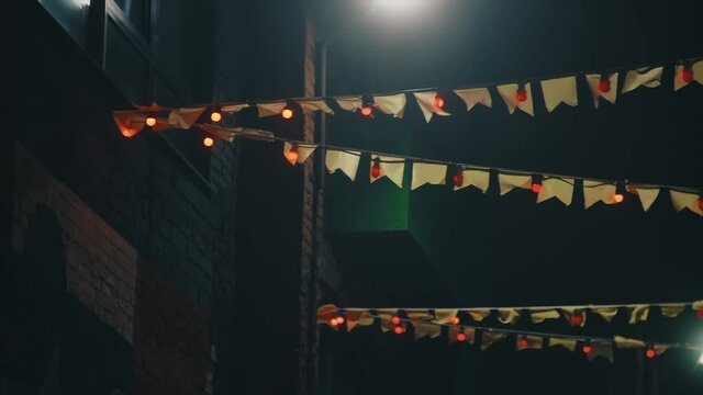 Small flags garland, chinese decoration against night sky and building. Video. Beautiful flags and lamps garlands hanging on the rope one by one.