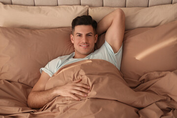 Fototapeta premium Man lying in bed with brown linens at home, above view
