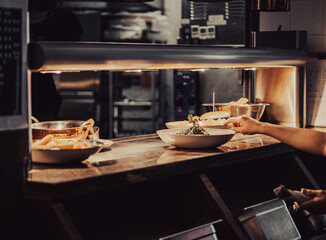 A food waiter picks up a plate from a food serving counter. The plates and bowls under the light are waiting