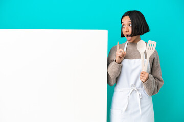 Young mixed race cook woman with a big placard isolated on blue background thinking an idea pointing the finger up