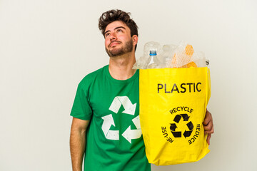 Young caucasian man recycling plastic isolated on white background dreaming of achieving goals and...
