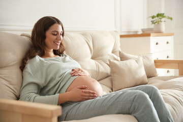 Fototapeta premium Happy pregnant woman touching her belly indoors