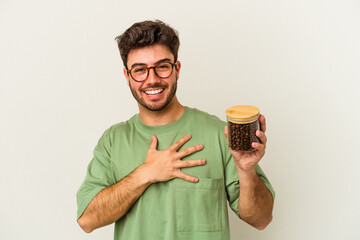 Young caucasian man holding a coffee jar isolated on white background laughs out loudly keeping hand on chest.