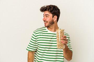 Young caucasian man holding chickpeas jar isolated on white background looks aside smiling, cheerful and pleasant.