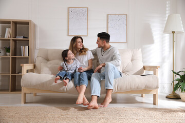 Happy family with little daughter sitting on sofa in living room - Powered by Adobe