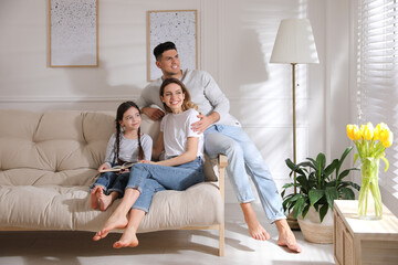 Happy family with little daughter sitting on sofa at home