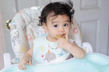 Portrait of a happy cute little Asian baby girl siting on baby dining table, mouth stained with foodlooking at camera