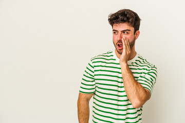Obraz premium Young caucasian man isolated on white background is saying a secret hot braking news and looking aside
